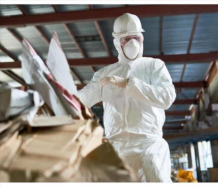 Low angle portrait of factory worker wearing biohazard suit sorting reusable cardboard at waste treatment plant, copy space
